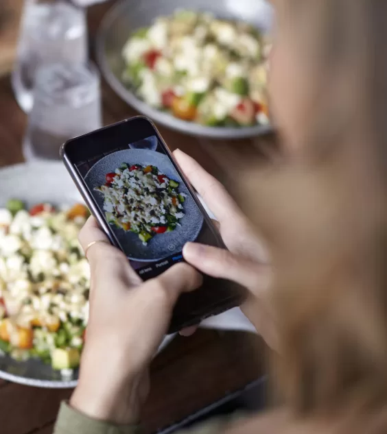 Female Friends In Restaurant Taking Picture Of Food In Restaurant To Post On Social Media